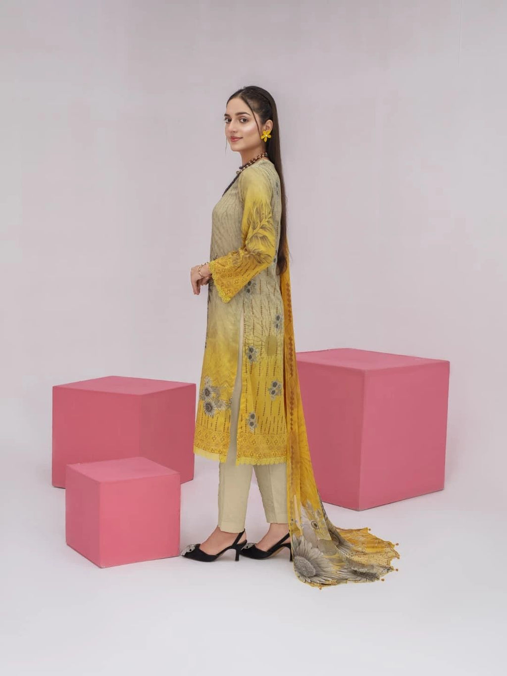 Woman in a yellow and green traditional outfit standing between pink cubes on a white background