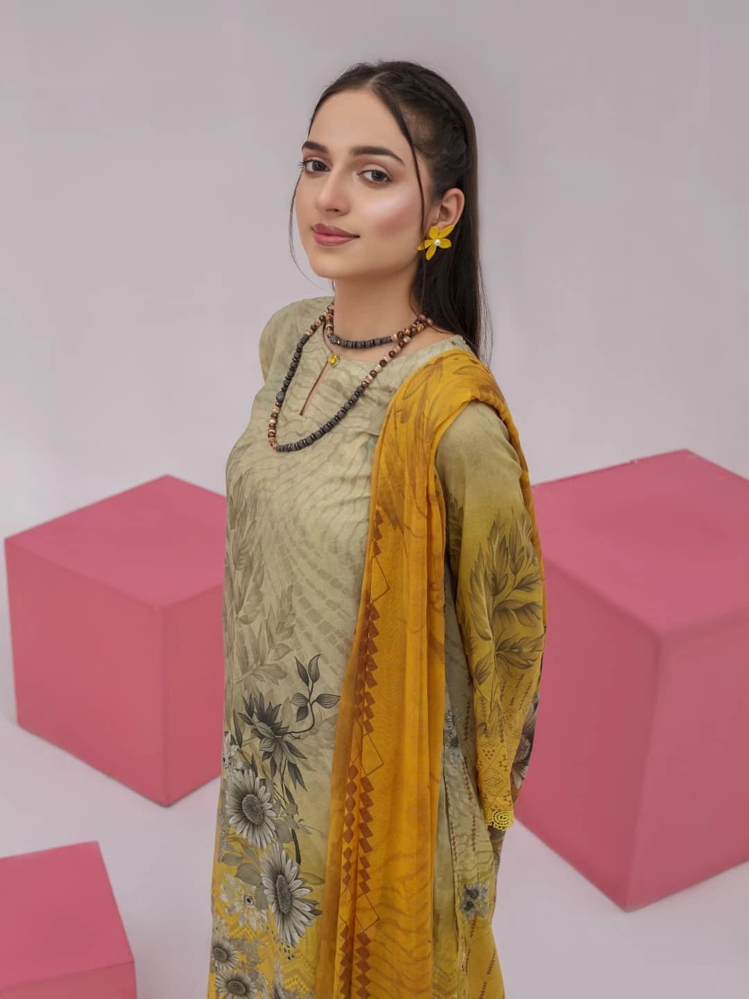 Woman wearing a green and yellow traditional outfit with pink geometric shapes in the background